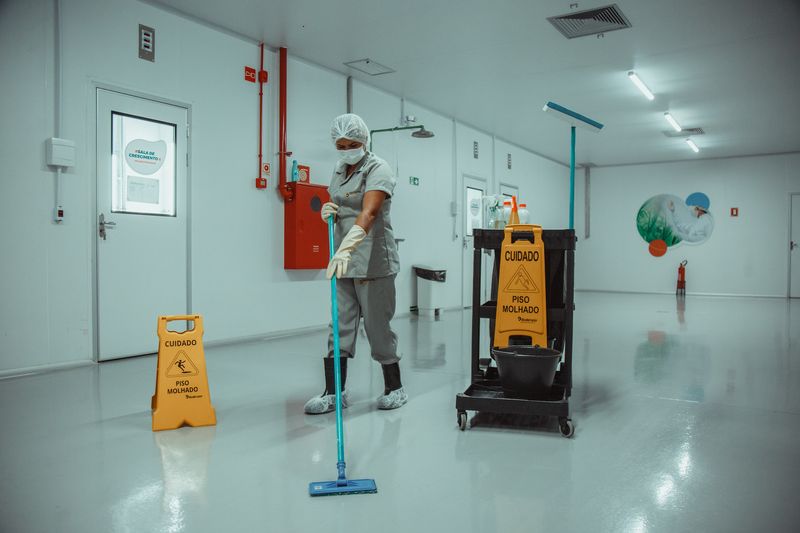 Profissional de limpeza do Grupo Distrital com EPI completo higienizando corredor hospitalar