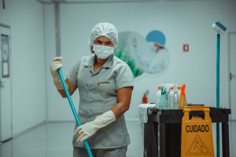Profissional com touca e máscara higienizando ambiente controlado