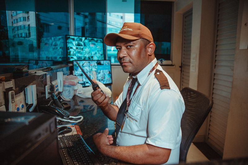 Porteiro do Grupo Distrital na guarita, operando o controle de acesso com rádio e monitores