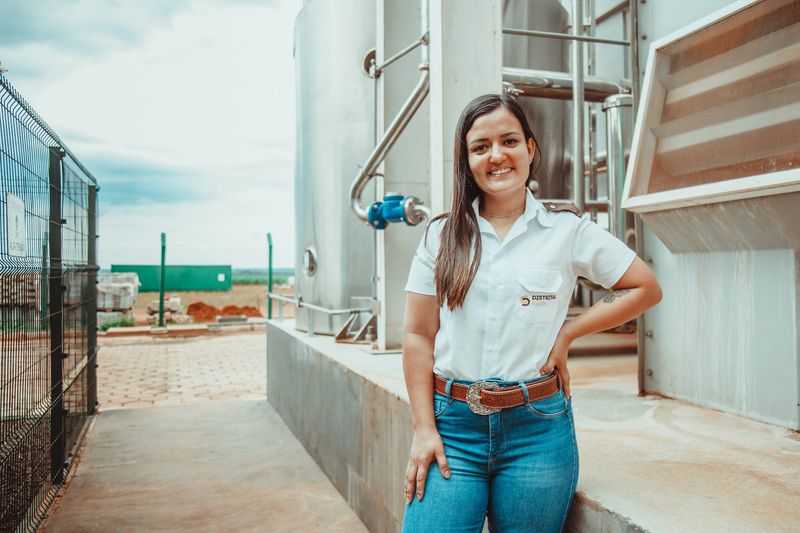 Colaboradora do Grupo Distrital em planta industrial com tanques ao fundo